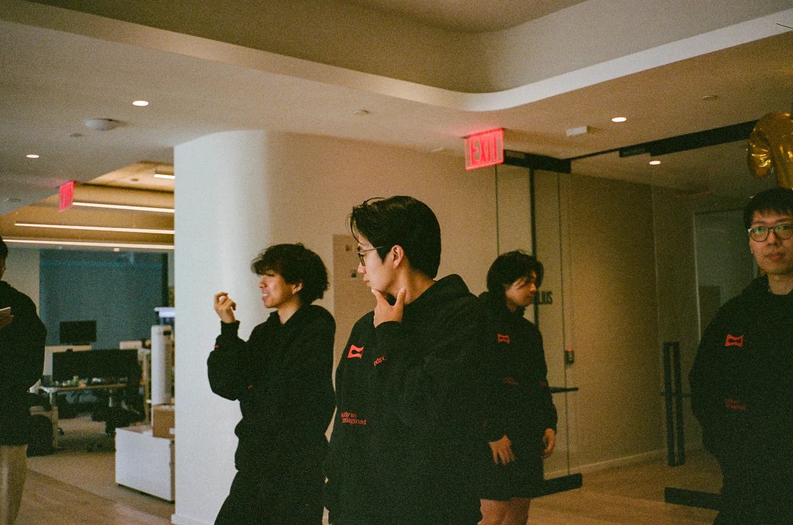 Melius team members in black hoodies gathered and talking in the office.