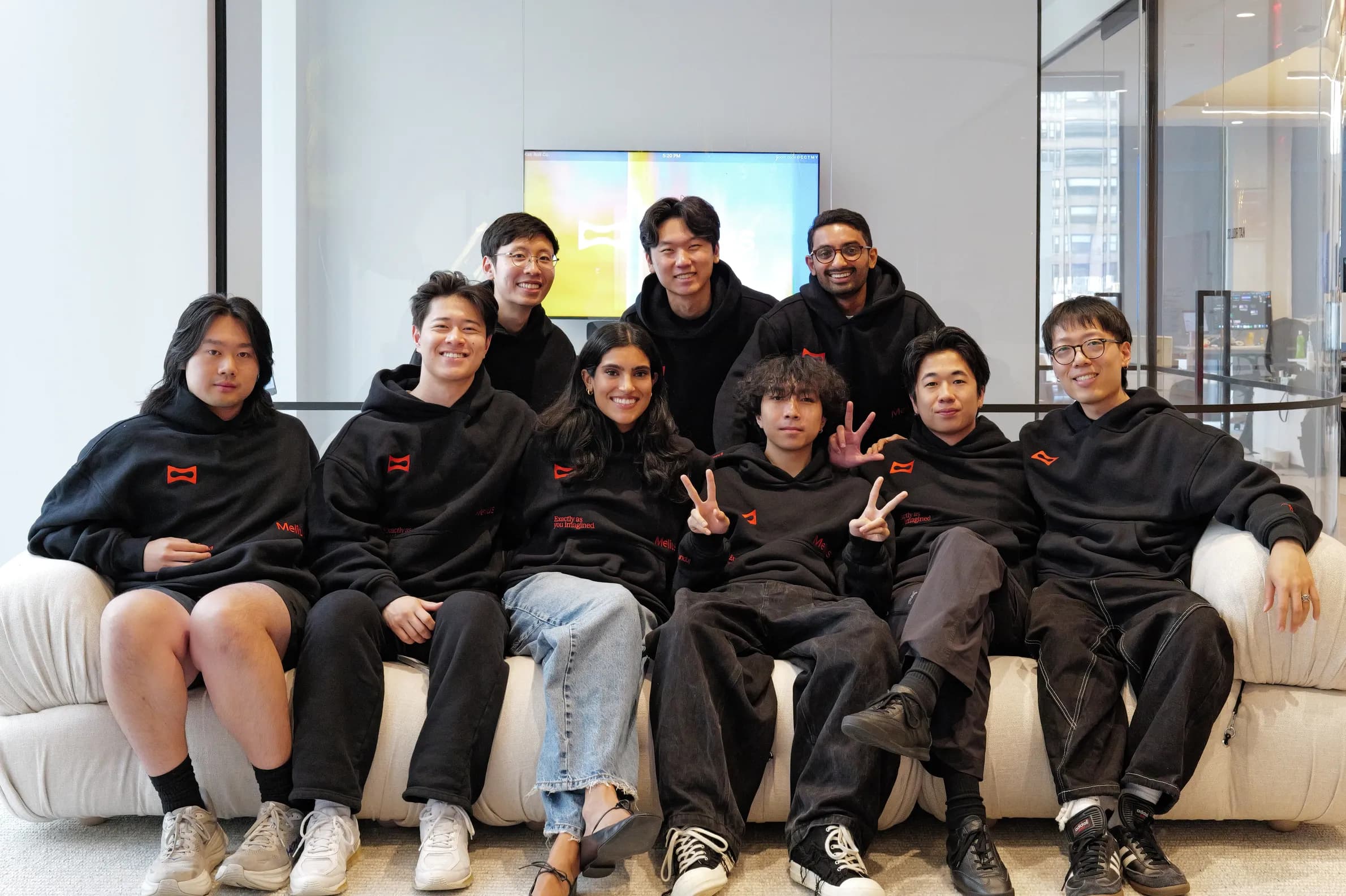 The Melius team in matching black hoodies posing together on a couch in a bright office.