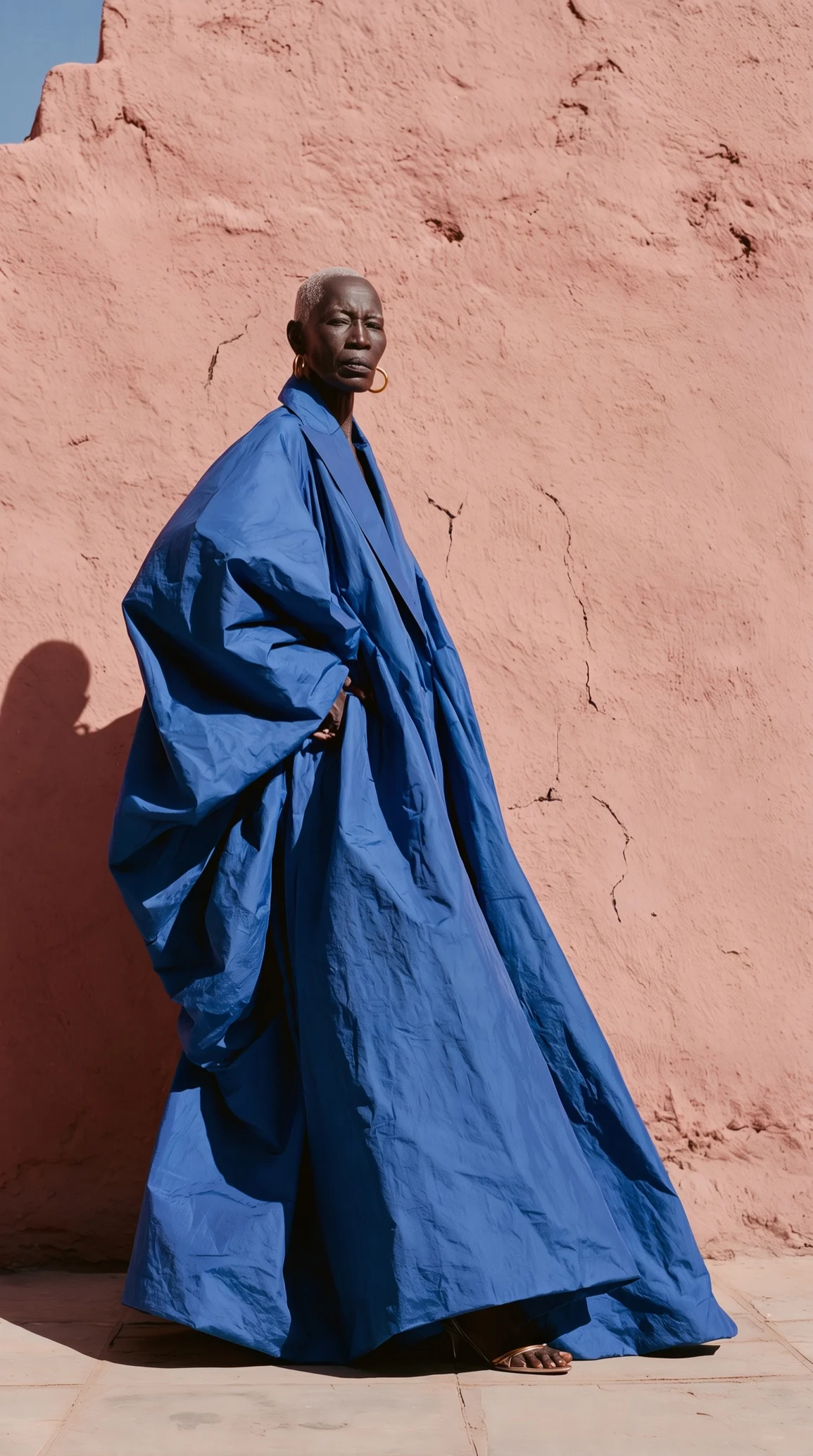 A man in a flowing blue robe standing against a pink wall