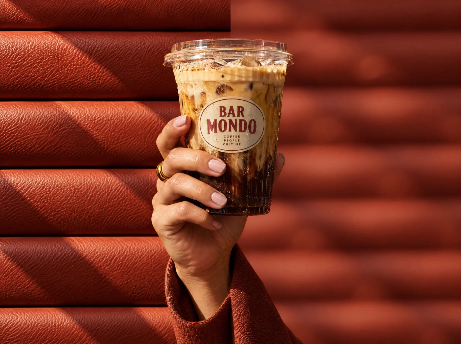 An iced coffee held against terracotta slats, sharp and then blurred