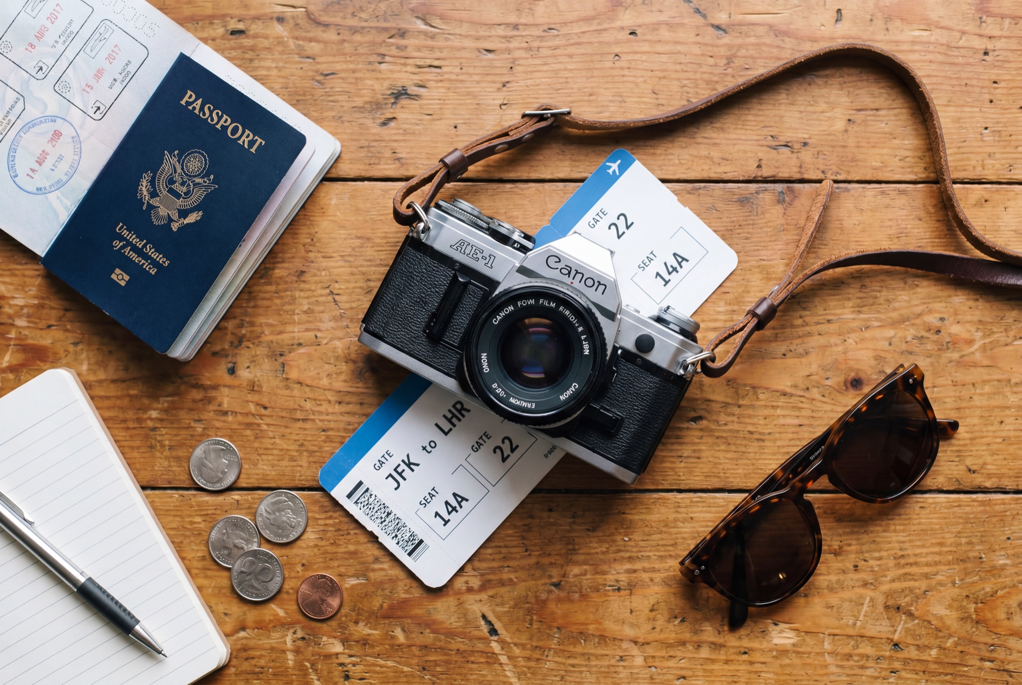 Travel flat-lay generated by Nano Banana Pro: passport, film camera, boarding pass reading JFK to LHR, GATE 22, seat 14A, sunglasses and coins on a wooden table